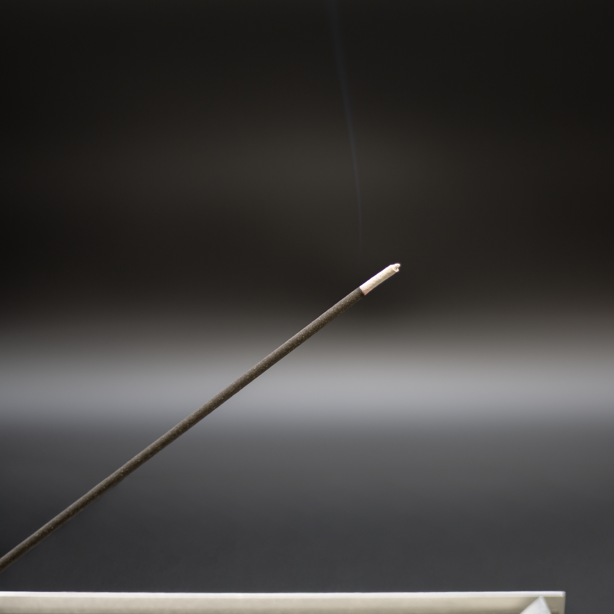 Burning charcoal incense stick with a faint plume of smoke