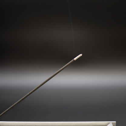 Burning charcoal incense stick with a faint plume of smoke