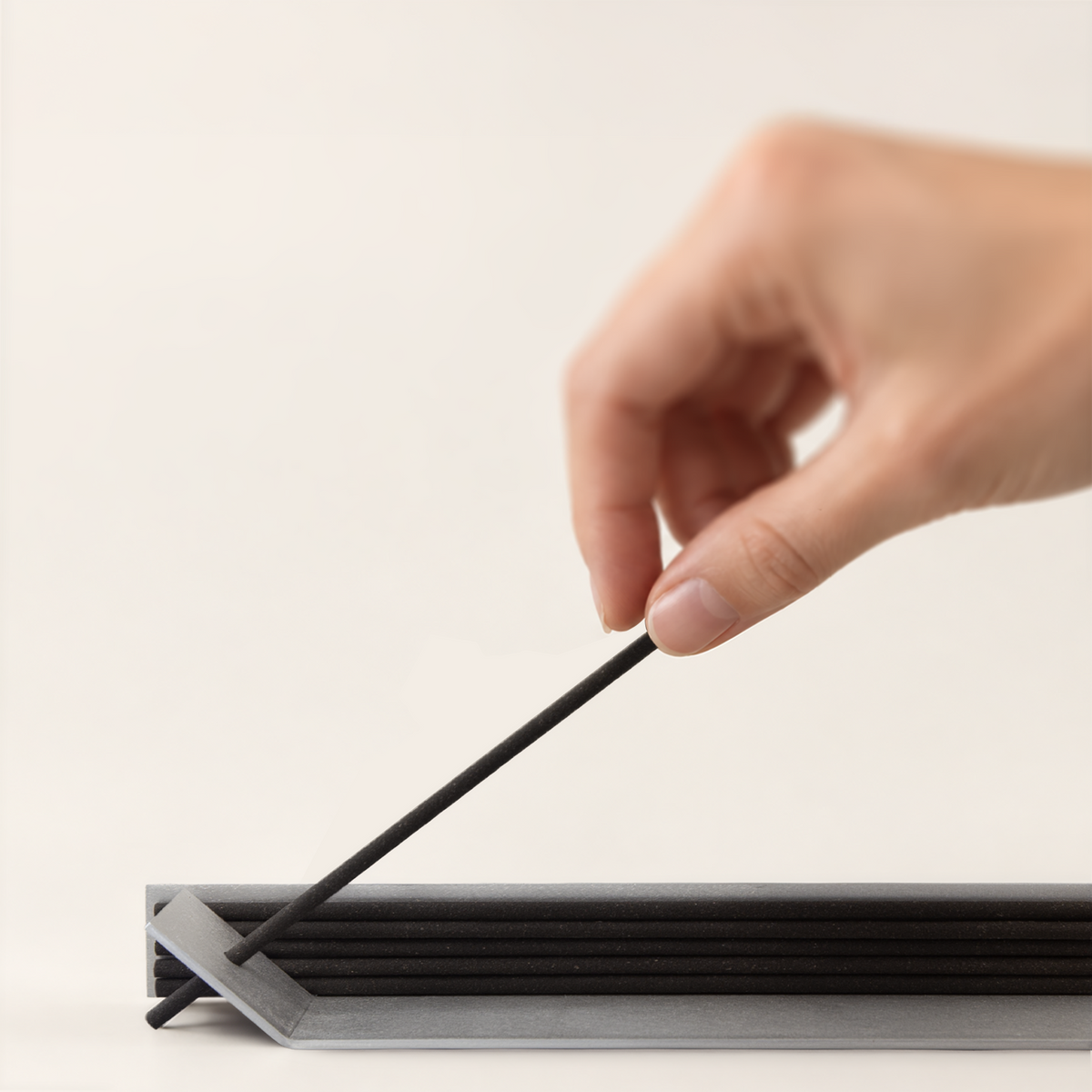 Close-up of a hand inserting an incense stick into the aluminum holder