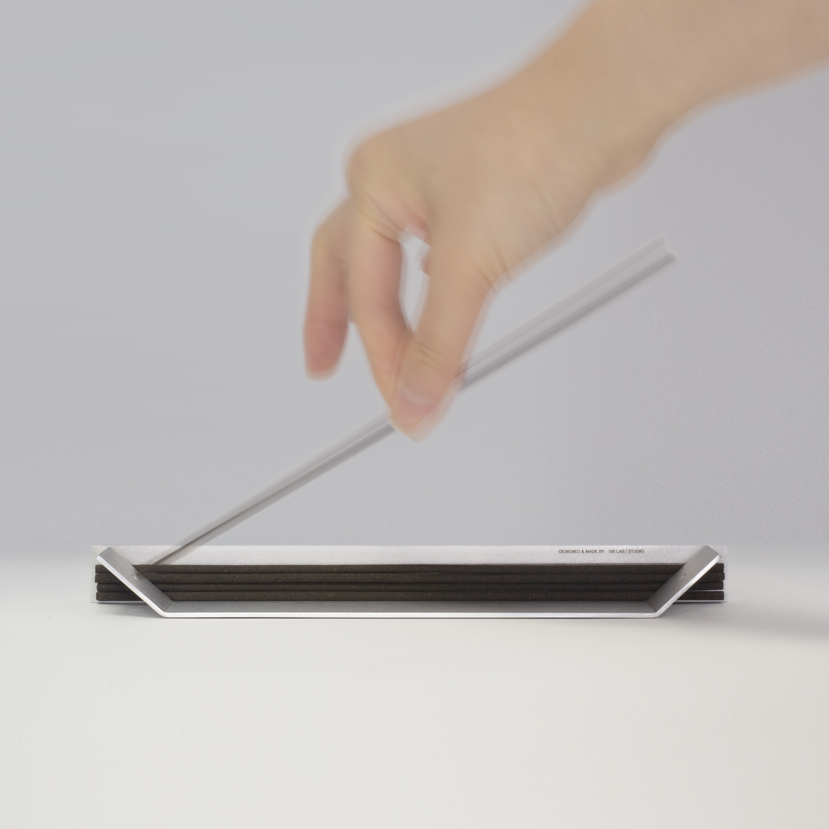Hand placing an incense stick in the folded aluminum holder